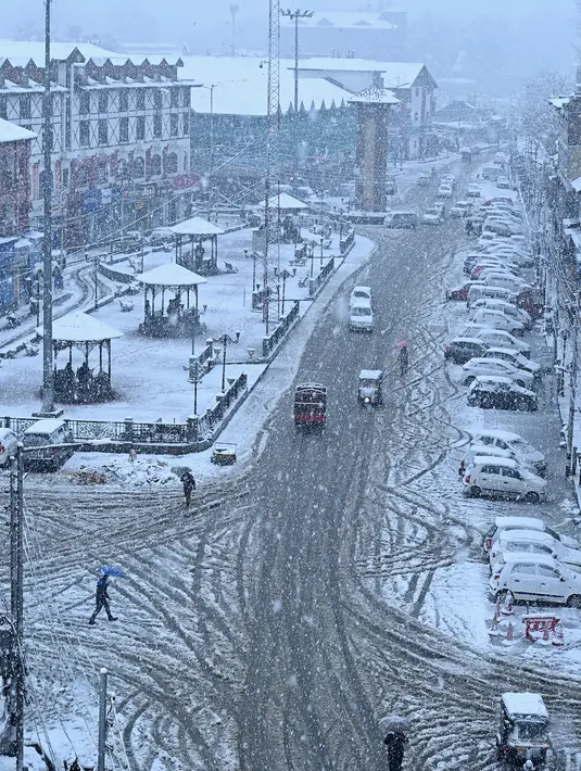 Orang-orang melintasi jalan yang tertutup salju di kota utama Kashmir, Srinagar, Kamis (7/11/2019). Srinagar menyambut salju pertama musim ini yang mulai turun. (Photo by Tauseef MUSTAFA / AFP)