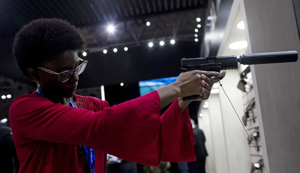 Seorang wanita memegang pistol dengan peredam di Pameran Internasional Pertahanan dan Keamanan LAAD di Rio de Janeiro, Brasil, Selasa, 11 April 2023. (AP Photo/Bruna Prado)