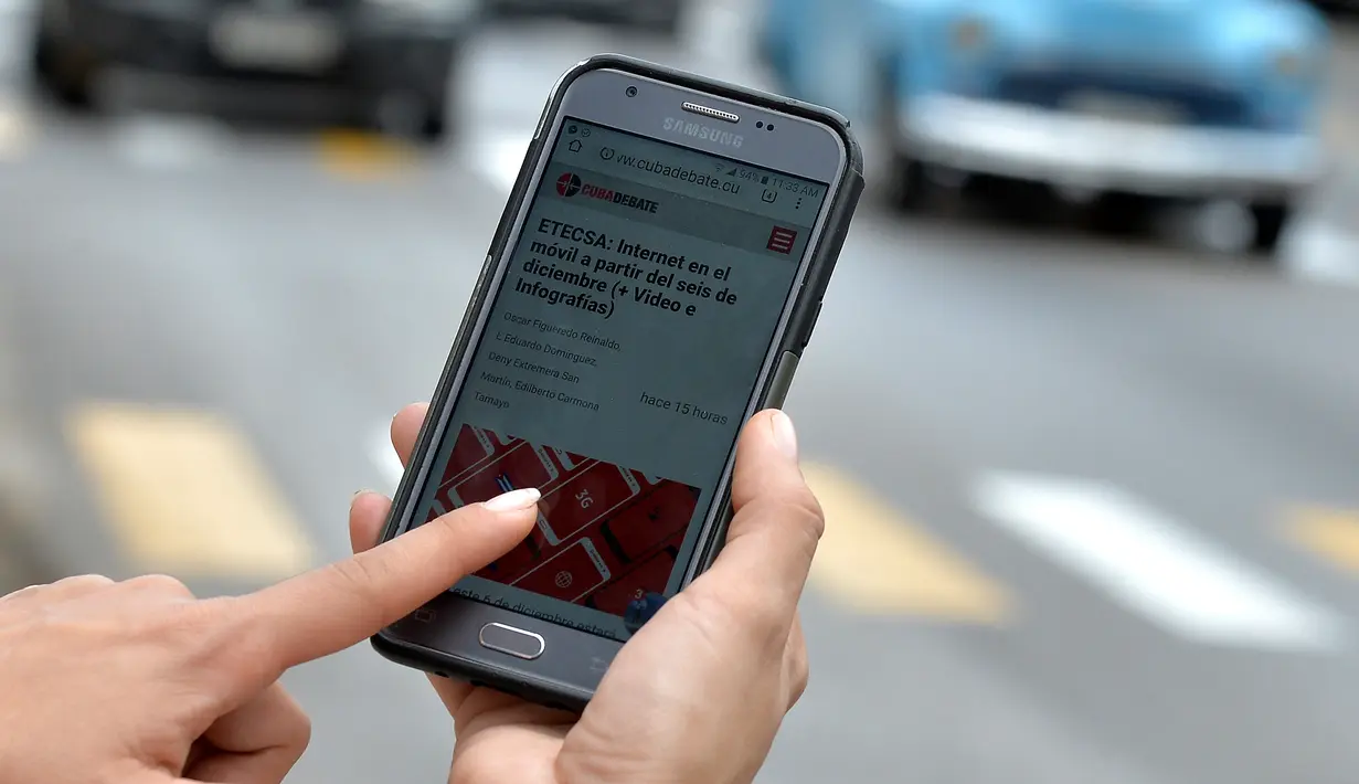 Seorang wanita menggunakan ponselnya untuk terhubung ke internet melalui WiFi di Havana, Rabu (5/12). Pemerintah Kuba mengumumkan bahwa masyarakat bisa mengakses internet secara bebas di ponsel mereka mulai Kamis ini. (YAMIL LAGE/AFP)