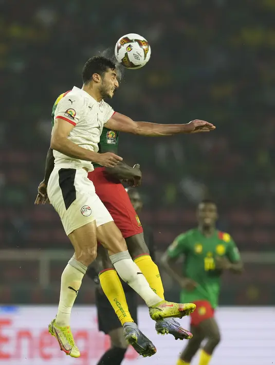 Bek Mesir, Mohamed Abdel-Moneim melompat saat berebut bola dengan penyerang Kamerun Vincent Aboubakar pada laga semifinal Piala Afrika 2021 di Paul Biya Stadium, Jumat (4/2/2022) dini hari WIB. Mesir sukses mengalahkan Kamerun 3-1 via drama adu penalti.  (AP Photo/Themba Hadebe)