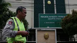 Seorang anggota kepolisian berjaga di depan PN Jakarta Utara, Senin (12/12). Ada dua mobil patroli polisi di depan gedung jelang sidang perdana Basuki Tjahaja Purnama (Ahok), namun belum ada penjagaan mencolok di lokasi.  (Liputan6.com/Johan Tallo)