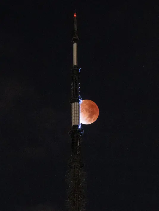 Bulan terlihat saat gerhana bulan di belakang One World Trade Center di New York , Jumat dini hari (19/11/2021). Gerhana bulan yang diamati pada tanggal 18 dan 19 November di berbagai wilayah dunia ini merupakan gerhana parsial yang terpanjang pada abad ini. (Yuki IWAMURA / AFP)