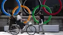 Orang-orang berjalan di dekat cincin Olimpiade yang dipasang di jembatan Nippon Bashi di Tokyo pada , Kamis (15/7/2021). Upacara pembukaan Olimpiade Tokyo akan digelar pada 23 Juli 2021 dan berakhir pada 8 Agustus 2021. (AP Photo/Hiro Komae)
