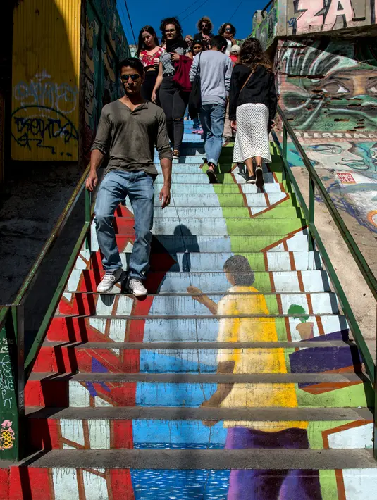 Turis berjalan menuruni tangga yang dihiasi mural jalanan di Valparaiso, Chile, 22 April 2019. Para seniman menuangkan kreativitas mereka di tangga, jalan-jalan labirin, dan lorong-lorong berbatu di Valparaiso. (Martin BERNETTI/AFP)