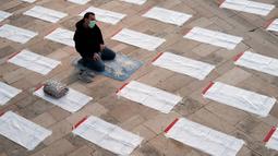 Seorang pria yang mengenakan masker berdoa di sebelah ruang yang telah ditentukan sebelumnya, dengan menerapkan pembatasan sosial yang diberlakukan untuk mencegah penyebaran Covid-19 sebelum salat Idul Fitri, di Masjid Agung Durres, Albania pada 24 Mei 2020. (Photo by Gent SHKULLAKU / AFP)