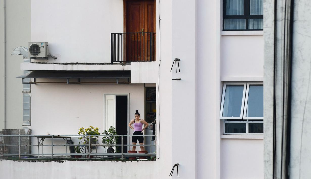 Gambar pada 4 September 2021 menunjukkan seorang perempuan berolahraga di balkon rumahnya di Hanoi, Vietnam, selama lockdown Covid-19. Menghadap ke jalan yang sepi, balkon kecil mereka menjadi saksi bisu terkait aktivitas yang dilakukan oleh masing-masing keluarga. (Nhac NGUYEN/AFP)