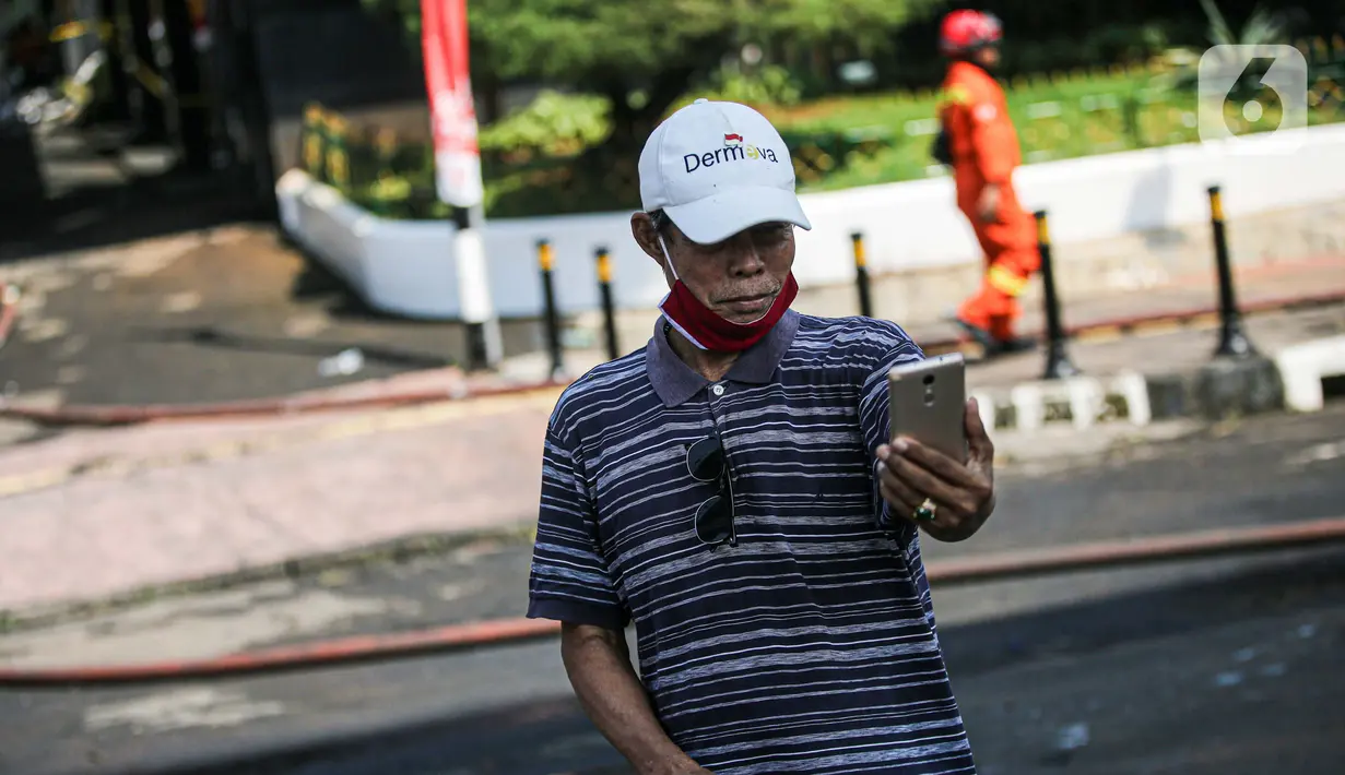 Seorang pria berswafoto dengan latar belakang gedung utama Kejaksaan Agung RI yang terbakar di Jalan Sultan Hasanuddin, Jakarta, Minggu (23/8/2020). Banyak warga yang memadati Jalan Hasanuddin untuk melihat langsung kondisi gedung Kejaksaan Agung yang hangus dilalap api. (Liputan6.com/Faizal Fanani)