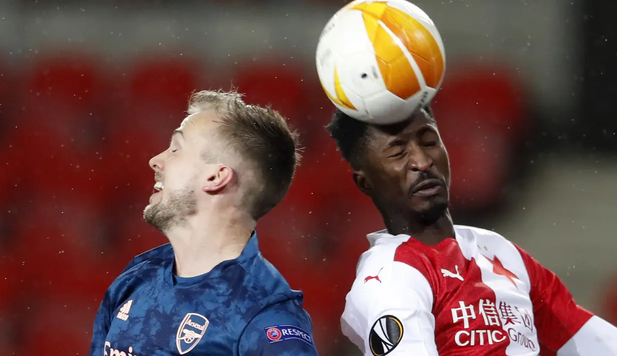 Penyerang Slavia Praha, Peter Olayinka menyundul bola melewati bek Arsenal, Rob Holding pada leg kedua perempat final Liga Europa di Stadion Sinobo, Praha, Jumat (16/4) dini hari WIB.  Arsenal lolos ke semifinal Liga Europa setelah menang telak 4-0 di markas Slavia Praha. (AP Photo/Petr David Josek)