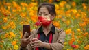 Seorang wanita mengenakan masker bertuliskan "I love you China" berpose untuk selfie dengan bunga mekar di taman umum di Beijing, Sabtu (2/10/2021). Pengunjung memadati taman dan lokasi wisata di Beijing saat China merayakan hari kedua masa libur Hari Nasional. (AP Photo/Mark Schiefelbein)