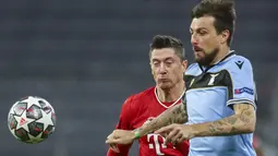 Penyerang Bayern Munchen, Robert Lewandowski dan bek Lazio, Francesco Acerbi berebut bola pada leg kedua babak 16 besar Liga Champions di Allianz Arena, Kamis dinihari WIB (18/3/2021). Munchen menang 2-1 atas tamunya Lazio dan maju ke perempatfinal dengan agregat 6-2. (AP Photo/Matthias Schrader)