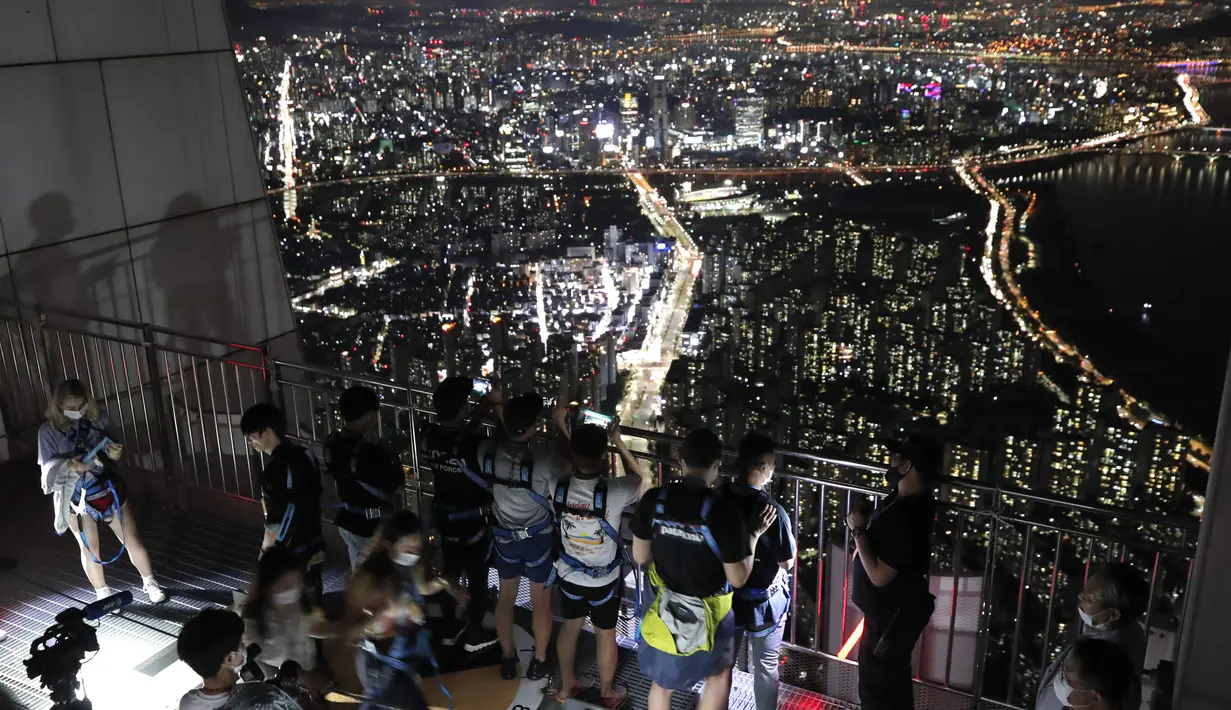Orang-orang yang memakai masker wajah untuk membantu melindungi dari penyebaran virus korona, melihat pemandangan malam Seoul saat mereka menginap di tempat berkemah semalam di atap gedung pencakar langit di Seoul, Korea Selatan (7/8/2020).  (AP Photo/Lee Jin-man)
