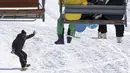 Pemain snowboard menuruni lereng saat dua orang lainnya duduk di kursi gantung di resor ski Tochal di kota Teheran, Iran (1/1/2022). Di tengah polusi udara dan kesengsaraan ekonomi, penduduk Teheran menemukan kenyamanan di resor ski di utara Teheran di pegunungan Alborz. (AP Photo/Vahid Salemi)