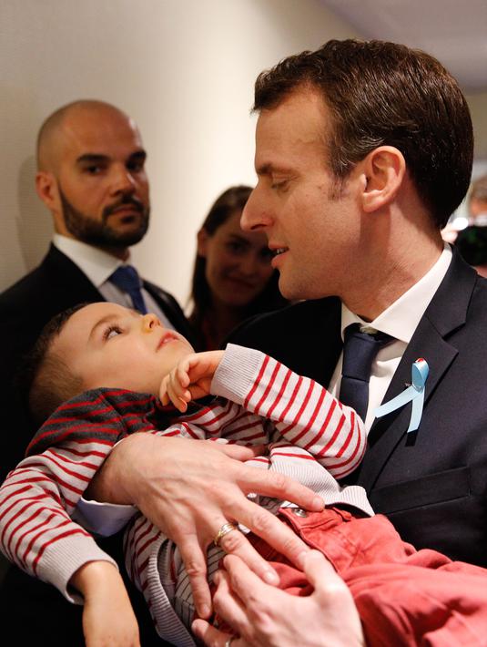 Presiden Prancis Emmanuel Macron menggendong seorang anak saat mengunjungi Graffiti's- Association Le Moulin Vert di Normandia, Prancis (5/4). Pada kunjungannya Presiden Emmanuel Macron berinteraksi dengan anak-anak autis.  (AP / Christophe Ena, Pool)