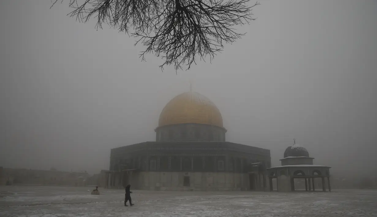 Seorang pria berjalan di dekat the Dome of the Rock atau Kubah Batu di kompleks Masjid Al Aqsa pada pagi bersalju di Kota Tua Yerusalem (18/2/2021). Salju yang mulai turun pada Rabu (17/2) malam juga menyelimuti kompleks Masjid Al-Aqsa. (AP Photo/Mahmoud Illean)