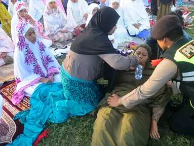 Anggota polisi dari Polda Bali membantu warga yang pingsan saat melakukan shalat Idul Fitri di Lapangan Pegok, Sesetan, Denpasar, Sabtu (22/4/2023). (merdeka.com/Arie Basuki)