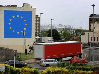 Kendaraan melintas dekat mural karya seniman jalanan Banksy di dekat terminal feri Dover, Kent, Inggris, Senin (8/5). Mural itu melukiskan seorang pria yang menaiki tangga dan menggugurkan salah satu bintang di bendera Uni Eropa. (Gareth Fuller/via AP)