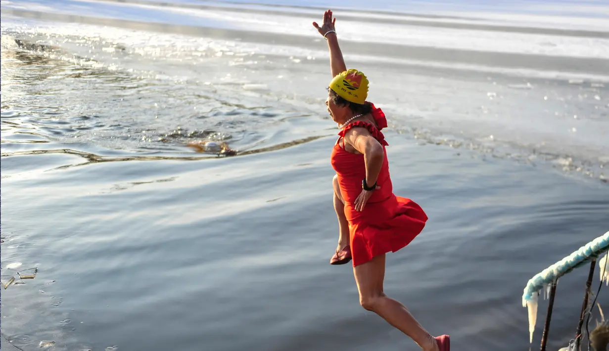 Seorang wanita melompat untuk berenang di danau  yang sebagaian beku dengan es saat suhu minus 20 derajat Celcius di Shenyang di provinsi Liaoning timur laut China (10/12). (AFP Photo/Str/China Out)