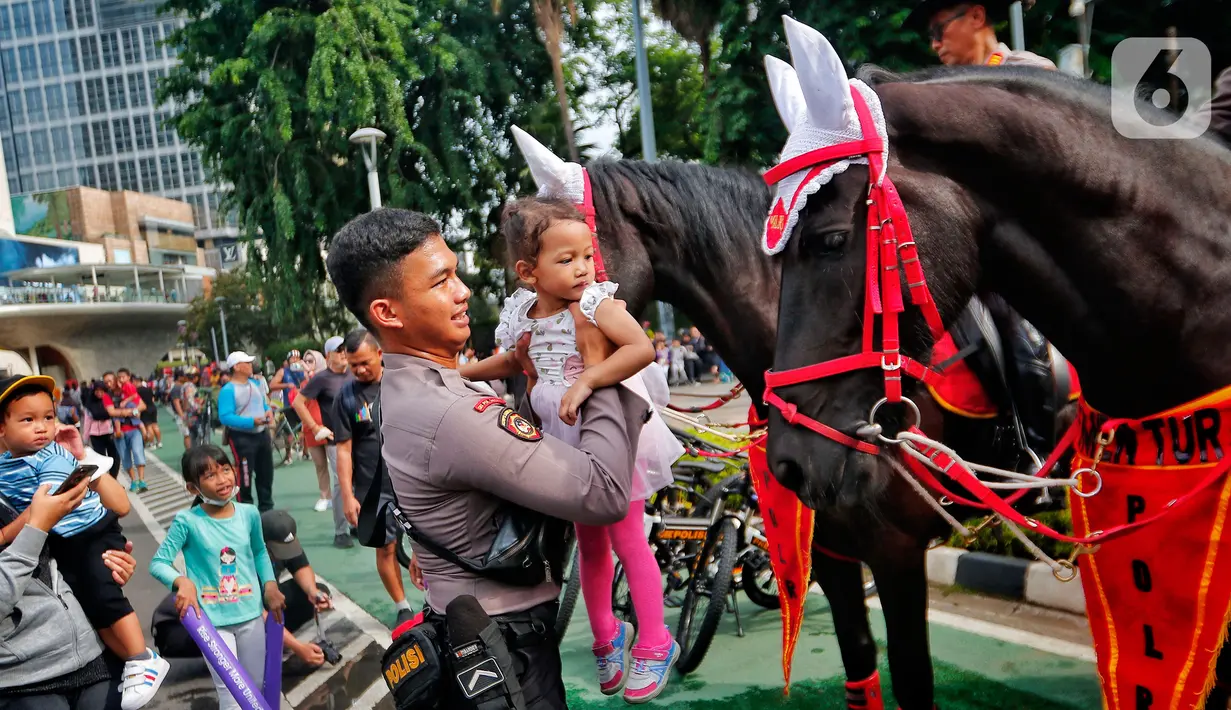 Polisi dari Detasemen Turangga Direktorat Polisi Satwa Polri menaiki seorang anak ke atas kuda saat Car Free Day (CFD) atau Hari Bebas Kendaraan Bermotor di kawasan Bundaran HI, Jakarta, Minggu (19/2/2023).Polisi berkuda selain ditugaskan untuk pengamanan simpatik juga untuk menghibur warga dan anak-anak saat Hari Bebas Kendaraan Bermotor serta memperkenalkan profesi tersebut kepada warga. (Lipitan6.com/Angga Yuniar)