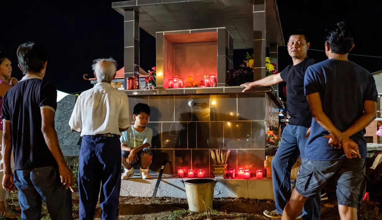 Sebuah keluarga Sino-Guianese berdiri di sekitar sebuah makam yang dihiasi bunga dan lilin di pemakaman Cayenne di Guyana Prancis (1/11). Perayaan ini adalah satu hari sebelum perayaan Peringatan Arwah Semua Orang Beriman. (AFP Photo/Jody Amiet)