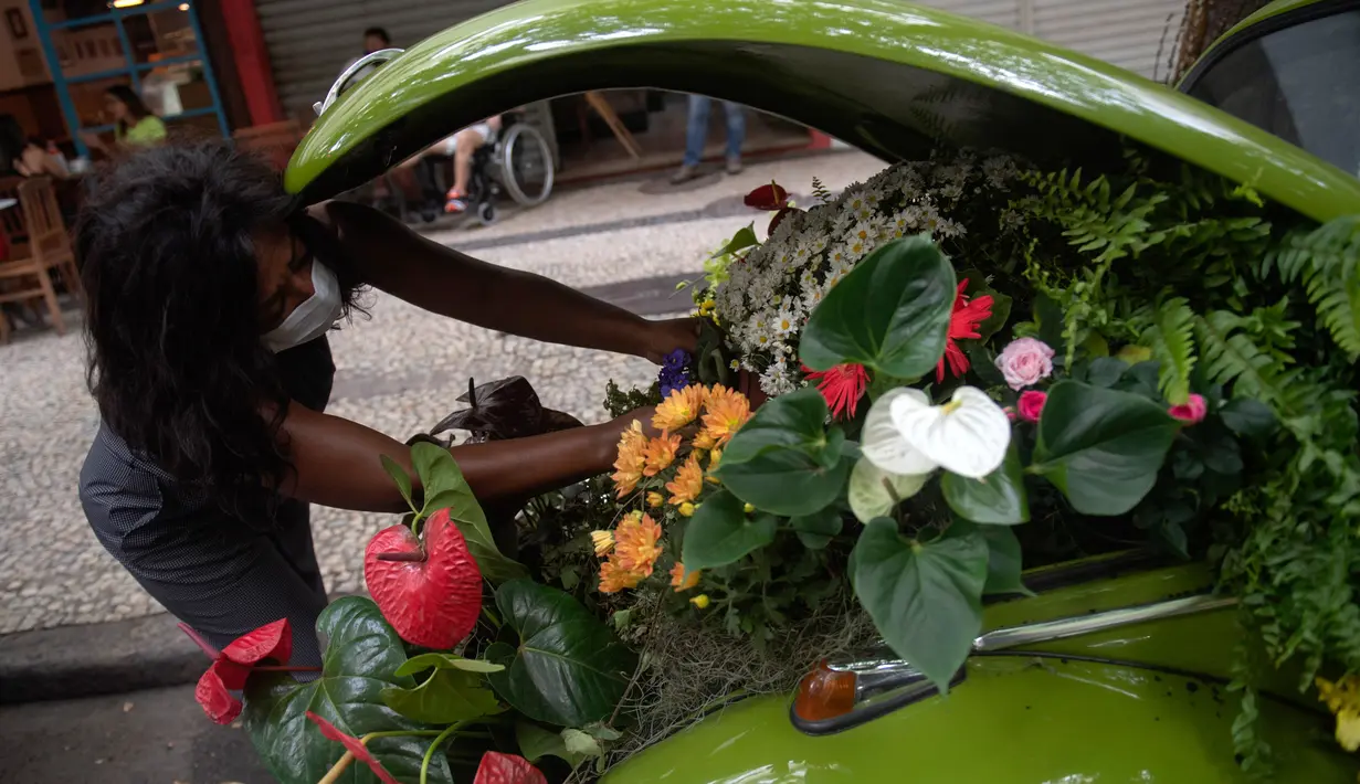 Roberta Machado dari Brasil menata bunga dan tanaman untuk dijual dengan Volkswagen Beetle 1969 yang diubah menjadi toko bunga keliling di Copacabana, Rio de Janeiro, Rabu (14/10/2020). Perempuan 51 tahun ini mengubah VW kodok untuk bertahan dari krisis akibat pandemi COVID-19. (MAURO PIMENTEL/AFP)