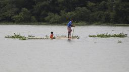 Seorang pria dan anak melakukan perjalanan dengan papan kayu melalui air banjir di daerah Bagha di Sylhet, Bangladesh (23/5/2022). Banjir bandang pra-musim telah membanjiri bagian dari India dan Bangladesh, menewaskan sedikitnya 24 orang dalam beberapa pekan terakhir dan mengirim 90.000 orang ke tempat penampungan. (AP Photo)
