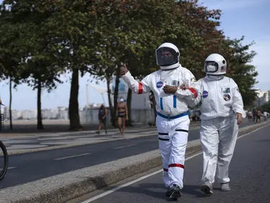 Akuntan Brasil Tercio Galdino (66) memberi isyarat jempol kepada warga yang mengendarai sepeda motor saat dia dan istrinya Alicea Galdino berjalan di sepanjang pantai Leme dengan pakaian pelindung mirip astronaut, Rio de Janeiro, Brasil, 12 Juli 2020. (Mauro Pimentel/AFP)