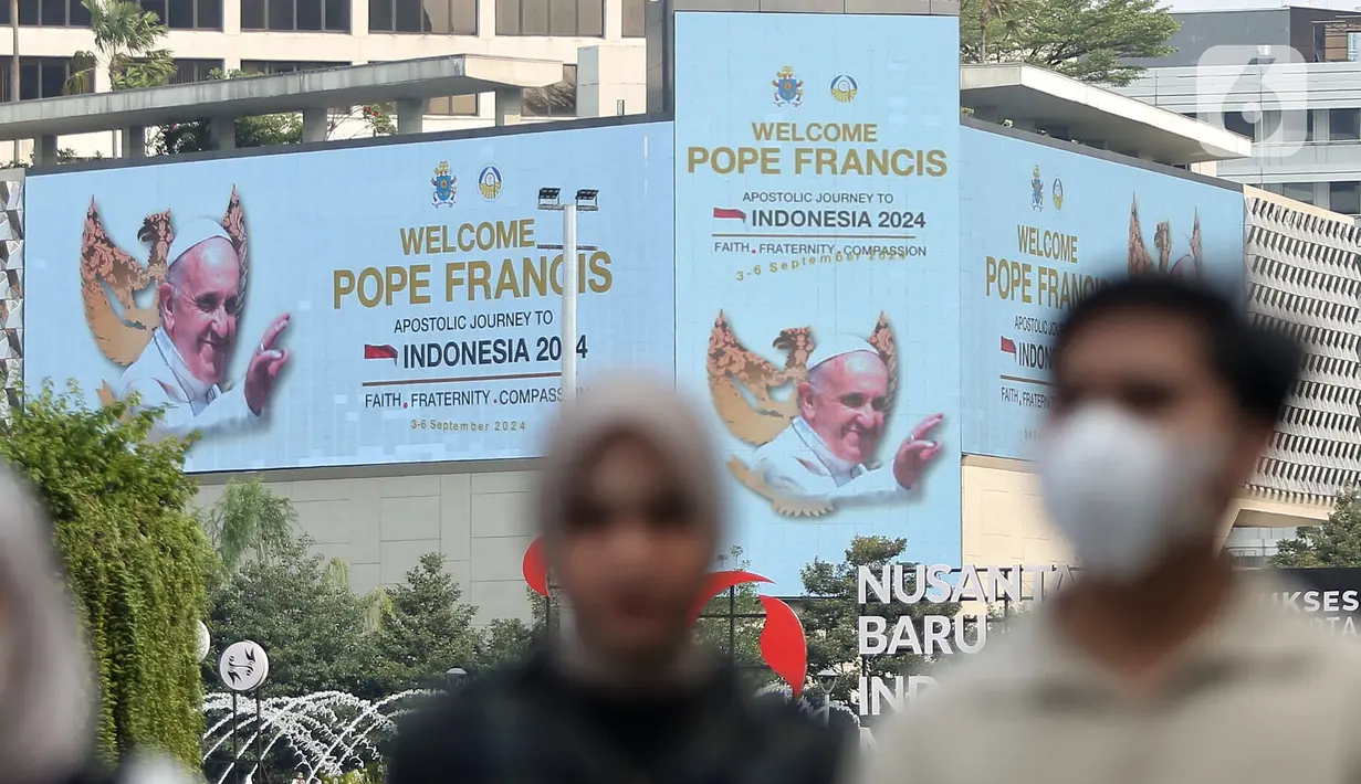 Warga berjalan di depan layar Light Emitting Diode (LED) yang bertuliskan ucapan selamat datang Pope Francis di kawasan Bundaran Hotel Indonesia, Jakarta, Minggu (1/9/2024). (Liputan6.com/Angga Yuniar)