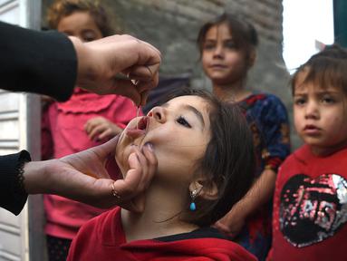 Tenaga kesehatan (kiri) memberikan vaksin polio kepada seorang anak selama kampanye vaksinasi di kawasan tua Kabul, Afghanistan pada 8 November 2021. Vaksinasi tersebut merupakan yang pertama sejak Taliban berkuasa di Afghanistan. (WAKIL KOHSAR / AFP)