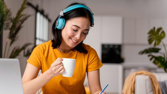 Seorang Wanita Sedang Journaling Sambil Mendengarkan Musik dan Minum Segelas Teh