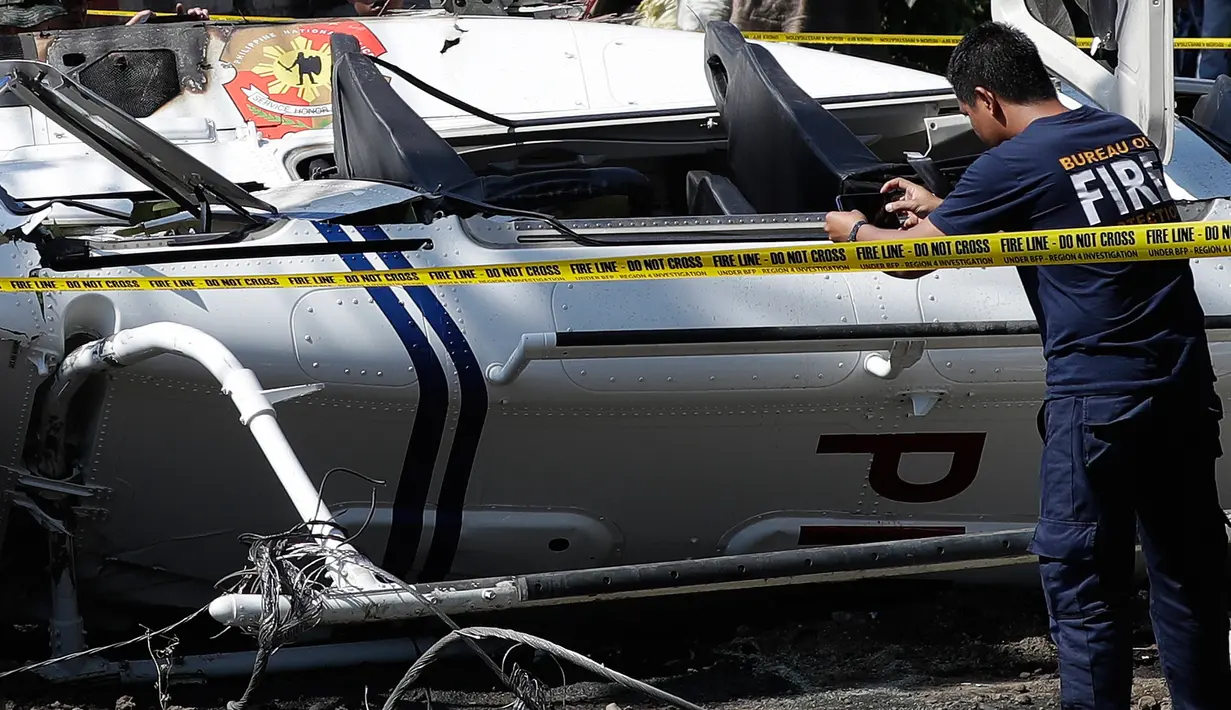 Seorang petugas mengambil gambar helikopter bell 429 yang membawa kepala polisi Filipina setelah jatuh di San Pedro, selatan Manila, Kamis (5/3/2020). Gangguan visibilitas menyebabkan helikopter menabrak kabel listrik dan kemudian jatuh. (AP/Aaron Favila)