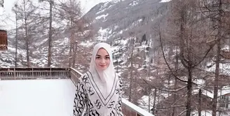Berpose di hamparan salju Swiss, istri Rezky Aditya ini tampak anggun berbalut dress dan hijab monokrom.