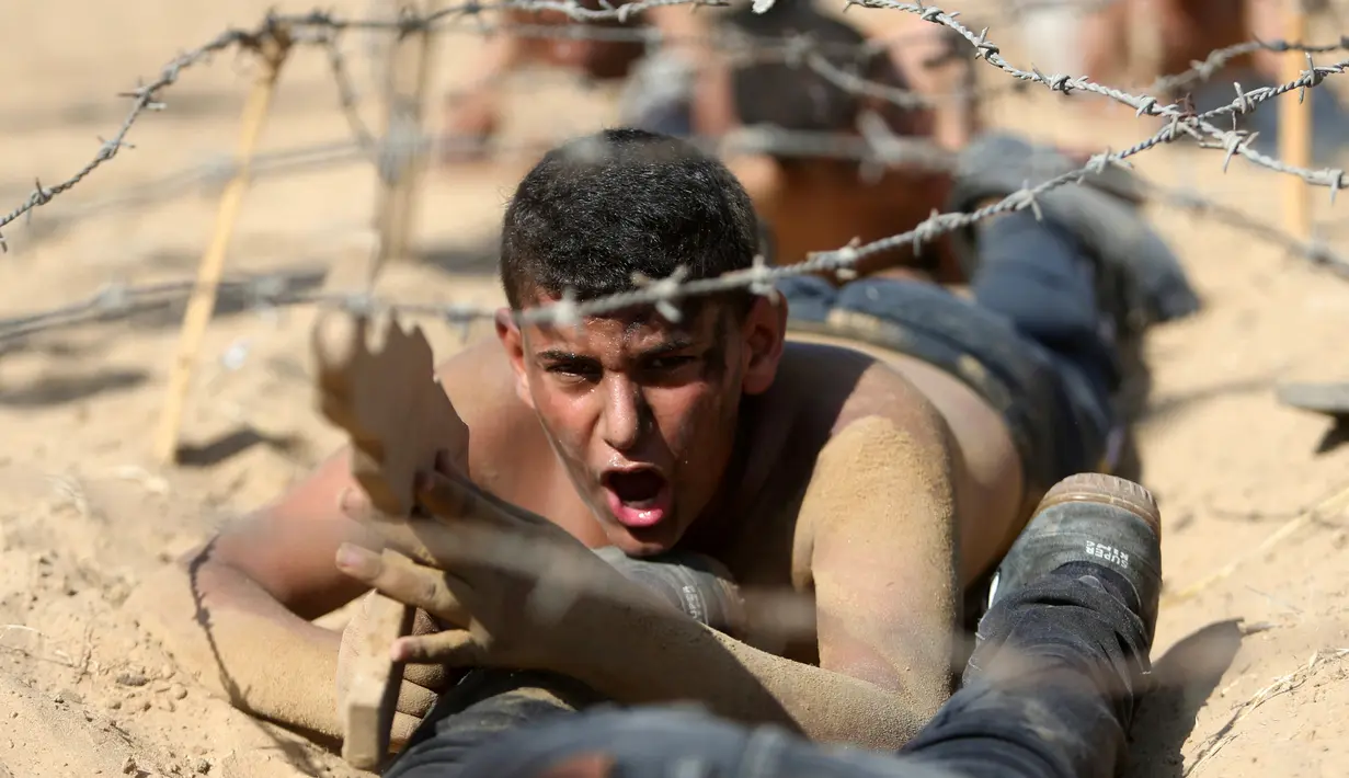 Seorang anak Palestina merangkak di bawah kawat berduri selama latihan militer di sebuah kamp musim panas yang diselenggarakan oleh Islamic Jihad Movement di Khan Younis di Jalur Gaza selatan (13/7). (REUTERS/Ibraheem Abu Mustafa)