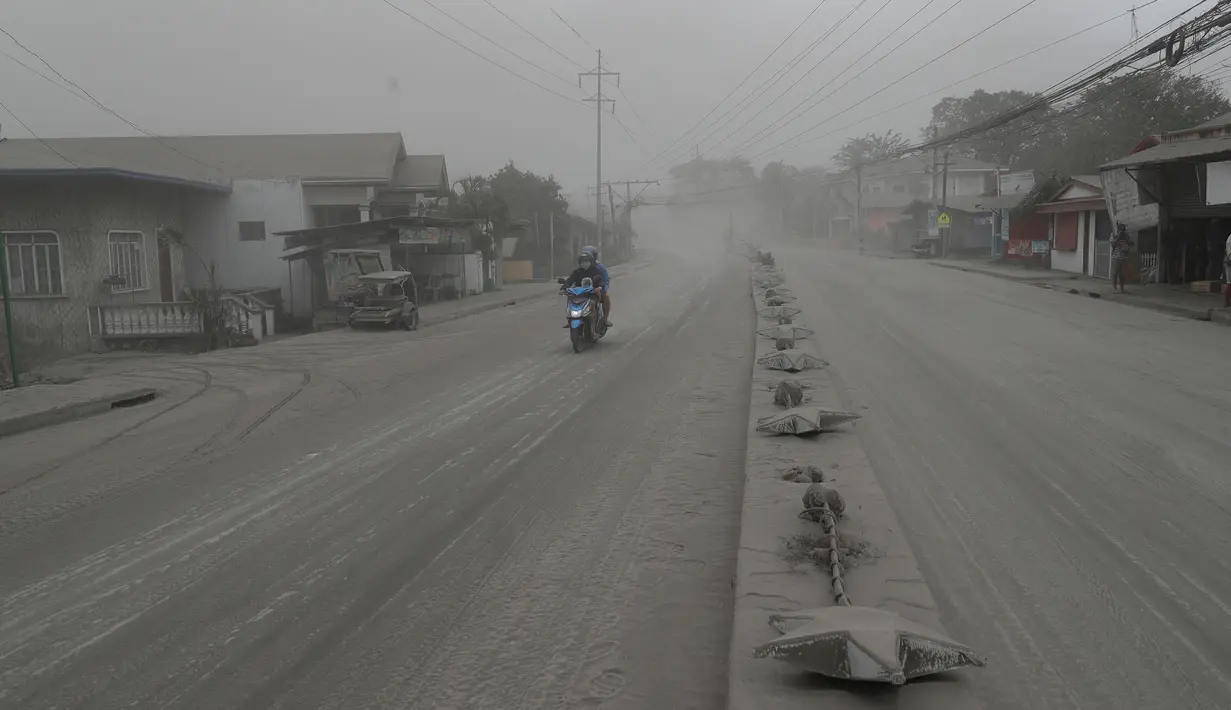 Pengendara sepeda motor melintasi jalan yang tertutup abu vulkanik dari gunung berapi Taal di Lemery, provinsi Batangas, Filipina, Senin (13/11/2020). Erupsi gunung Taal memaksa puluhan ribu orang mengungsi serta membuat sekolah-sekolah dan toko di Manila tutup. (AP/Aaron Favila)