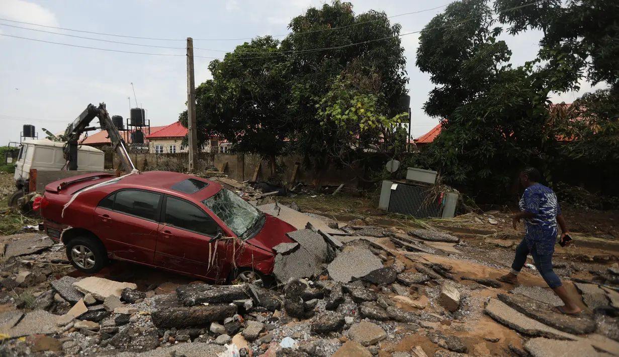 Seorang wanita berjalan melalui jalan yang terkena banjir bandang setelah hujan lebat di Trademoore Estate, Lugbe, Abuja, Nigeria (13/9/2021). Badan Manajemen Darurat Nasional Nigeria (NEMA) mengkonfirmasi 3 orang tewas, dan puluhan mobil dan rumah terkena dampak di malapetaka. (AFP/Kola Sulaimon)