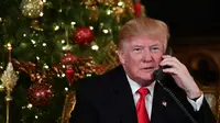 Ekspresi Presiden AS Donald Trump saat berbicara dengan anak-anak di telepon di Palm Beach, AS (24/12). Pada malam natal ini Trump dan istrinya sibuk mendengarkan permintaan anak-anak kepada Sinterklas. (AFP Photo/Nicholas Kamm)