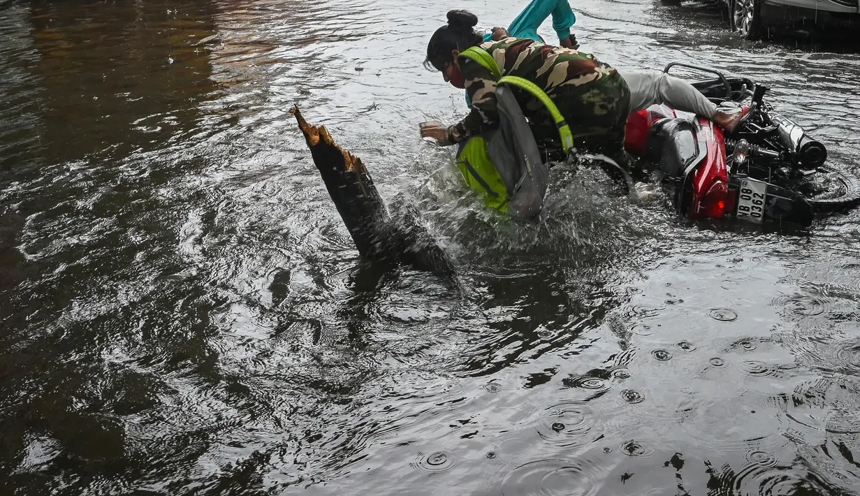 Seorang pengendara sepeda motor terjatuh saat melintasi jalan yang tergenang air setelah hujan deras di Kolkata (20/9/2021). Hujan dilaporkan dipicu oleh sirkulasi siklon yang terbentuk di atas Teluk Benggala. (AFP/Dibyangshu Sarkar)