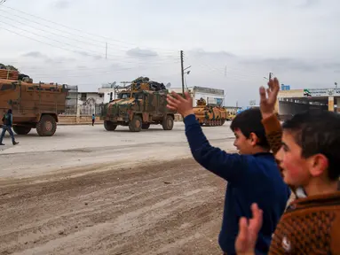 Sejumlah anak-anak melambaikan tangan ke iring-iringan pasukan lapis baja Turki (APC) yang melewati persimpangan perbatasan Bab al-Salamah antara Suriah dan Turki di utara provinsi Aleppo (21/1). (AFP/ Nazeer al-Khatib)