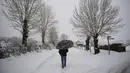 Seorang pria berlindung di bawah payung sambil berjalan di sepanjang jalan saat salju menutupi lanskap di Burguete, Spanyol utara, Senin, 16 Januari 2023. Pihak berwenang telah mengumumkan salju dan suhu sangat rendah selama beberapa hari ke depan di seluruh bagian utara negara itu. (AP Photo/Alvaro Barrientos)