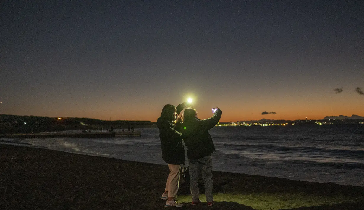 Dua wanita berfoto saat mereka menunggu matahari terbit di Pantai Selatan Chigasaki pada Hari Tahun Baru di Prefektur Kanagawa, barat daya Tokyo (1/1/2021). (AFP/Philip Fong)