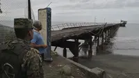 Seorang warga dan tentara Panama memandang ke arah jembatan kayu yang rusak pasca hantaman gempa magnitudo 6.1, Minggu 12 Mei 2019. (AP Photo)