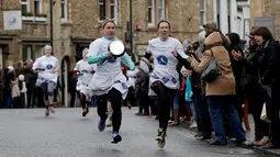 Peserta ambil bagian dalam lomba lari sembari membawa wajan berisi pancake di kota Olney, Inggris, Selasa (13/2). Perlombaan pancake yang biasanya diikuti oleh para wanita atau ibu-ibu ini sudah dimulai sejak tahun 1445. (AP Photo/Matt Dunham)