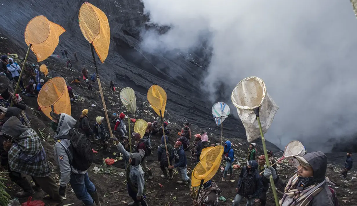 Orang-orang mencoba menangkap sesajen yang dilemparkan suku Tengger ke kawah Gunung Bromo saat upacara Yadnya Kasada di Probolinggo, Jawa Timur, Sabtu (26/6/2021). Suku Tengger mempersembahkan sesajen berupa beras, buah, ternak, dan barang lainnya untuk mencari berkah dari dewa. (Juni Kriswanto/AFP)
