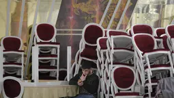 Seorang pria duduk dekat tumpukan kursi yang dipindahkan untuk menampung pengungsi yang melarikan diri dari invasi Rusia terhadap Ukraina, di dalam ballroom yang menjadi tempat penampungan pengungsi darurat di hotel & spa bintang 4, di Suceava, Rumania, 4 Maret 2022. (AP Photo/Andreea Alexandru)