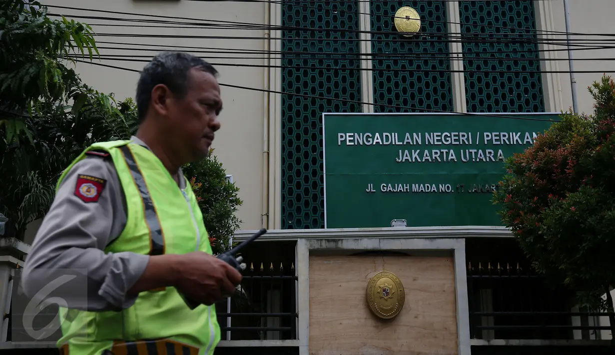 Seorang anggota kepolisian berjaga di depan PN Jakarta Utara, Senin (12/12). Ada dua mobil patroli polisi di depan gedung jelang sidang perdana Basuki Tjahaja Purnama (Ahok), namun belum ada penjagaan mencolok di lokasi.  (Liputan6.com/Johan Tallo)