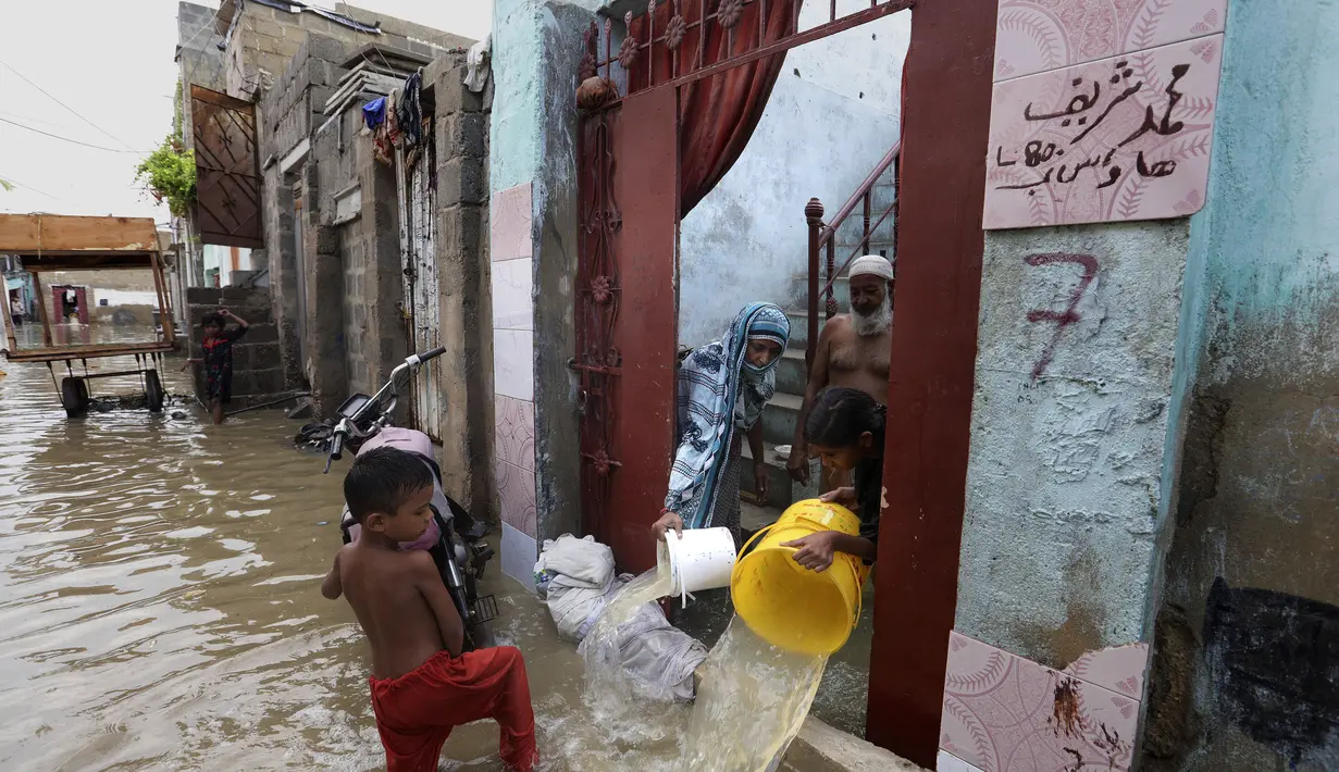 Sebuah keluarga mengeluarkan air banjir dari rumah mereka setelah hujan lebat di Karachi, Pakistan, Minggu, (26/7/2020). Tingginya banjir membuat air masuk ke rumah warga. (AP Photo/Fareed Khan)