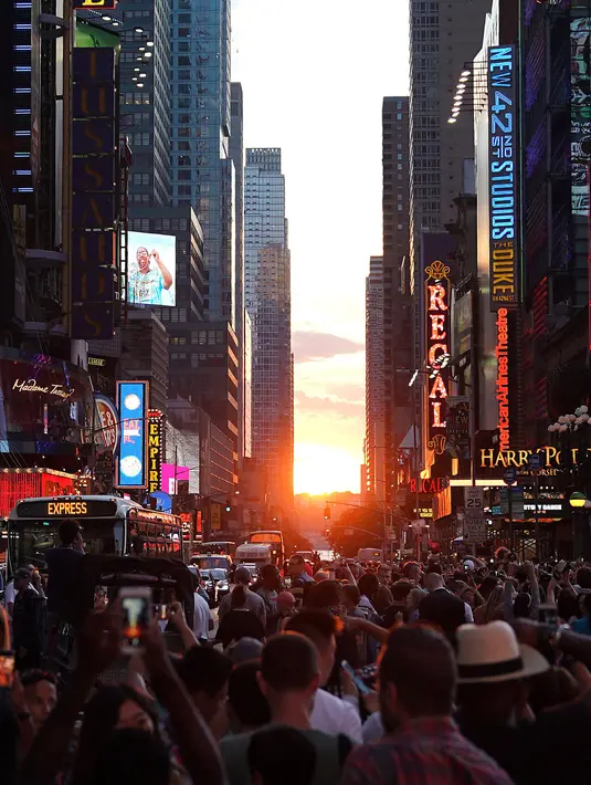 Orang-orang mengambil gambar matahari terbenam di antara pencakar langit ketika fenomena Manhattanhenge di 42nd street di Times Square, New York City, Kamis (12/7). Manhattanhenge dimana saat matahari terbenam sejajar dengan jalan. (AFP/TIMOTHY A. CLARY)