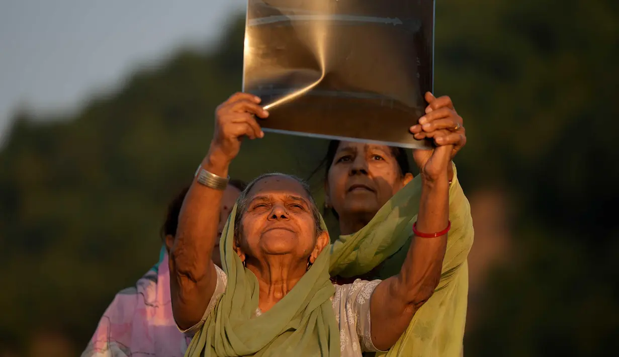 Perempuan menyaksikan Gerhana Matahari sebagian melalui film sinar-X di tepi Sungai Tawi, Jammu, India, Selasa (25/10/2022). Peristiwa Gerhana Matahari terakhir pada tahun 2022 terlihat dari sebagian besar Eropa, serta Afrika Utara, Timur Tengah, dan Asia Barat. (AP Photo/Channi Anand)