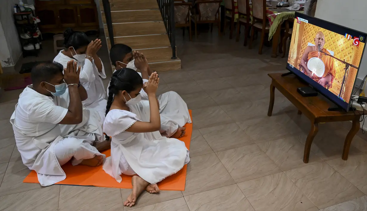 Sebuah keluarga Buddha mengikuti upacara keagamaan melalui televisi pada perayaan Hari Waisak selama penguncian wilayah di pinggiran Kolombo, Sri Lanka pada Rabu (26/5/2021). Hari Raya Waisak 2021 diperingati pada 26 Mei tahun ini. (ISHARA S. KODIKARA / AFP)