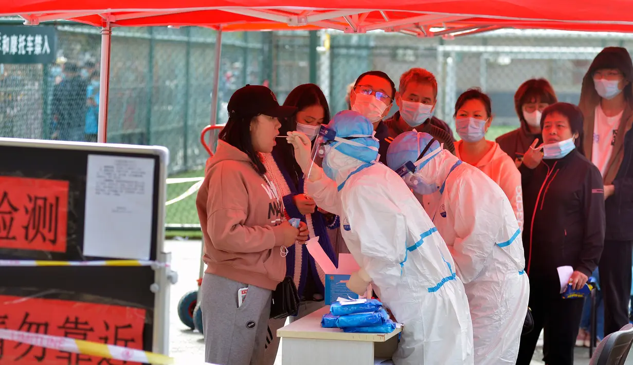 Petugas medis mengambil sampel warga saat yang lainnya antre untuk tes COVID-19 di dekat daerah perumahan di Qingdao, China, Senin (12/10/2020). Lebih dari 9 juta orang yang tinggal di kota Qingdao, menjalani tes virus Corona (COVID-19) secara massal setelah muncul kasus baru. (Chinatopix via AP)