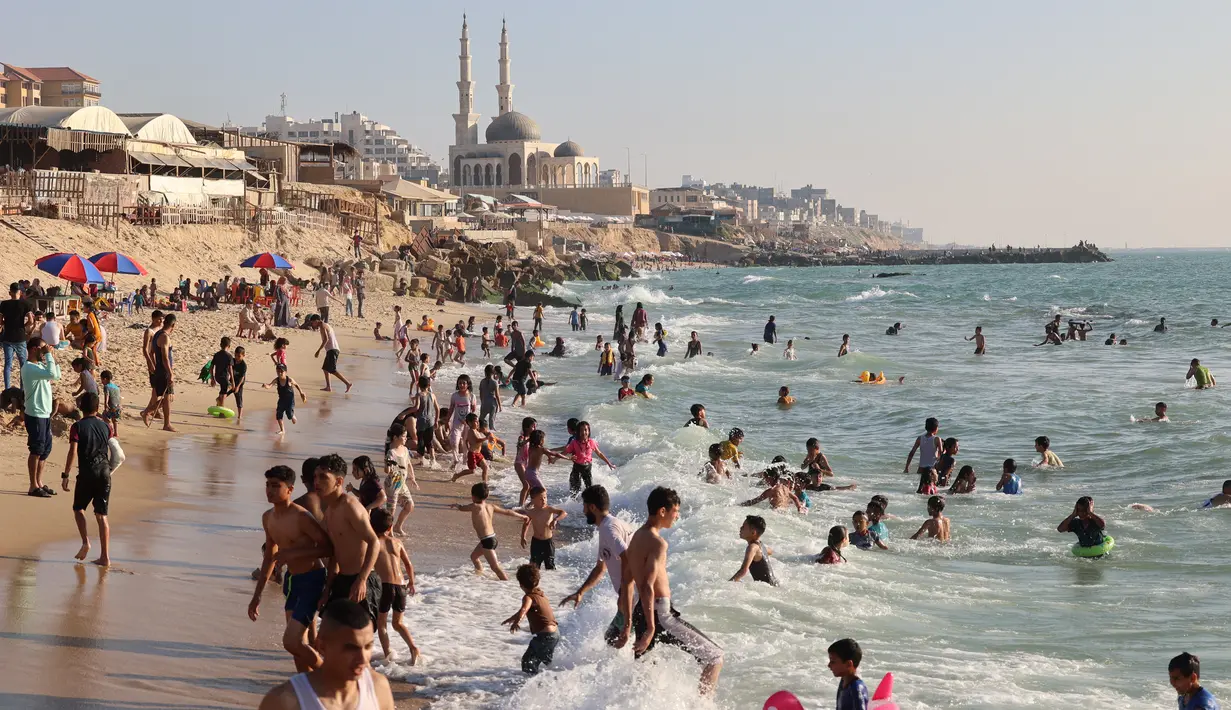 Warga Palestina bermain air di pantai Beit Lahia di Jalur Gaza utara saat para siswa memulai liburan musim panas mereka pada 3 Juni 2022. Sejumlah warga menikmati musim panas dengan berenang dan bermain air di pantai. (MOHAMMED ABED / AFP)